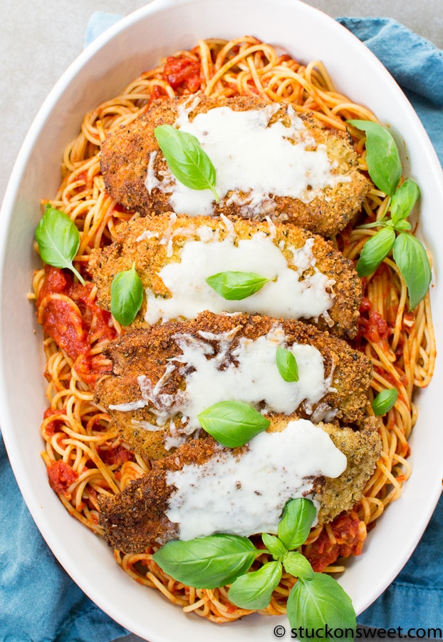 Breaded chicken parmesan over spaghetti with tomato sauce, topped with melted mozzarella and fresh basil leaves.