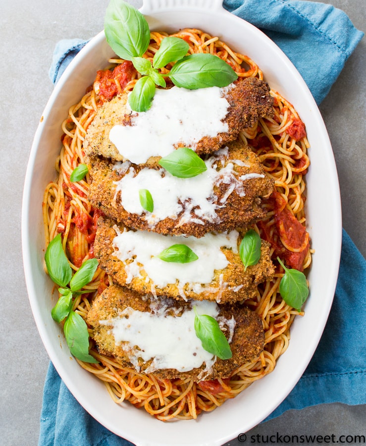 Crispy breaded chicken cutlets topped with creamy white sauce, served over a bed of spaghetti with tomato sauce, garnished with fresh basil leaves for a delicious Italian-inspired meal.