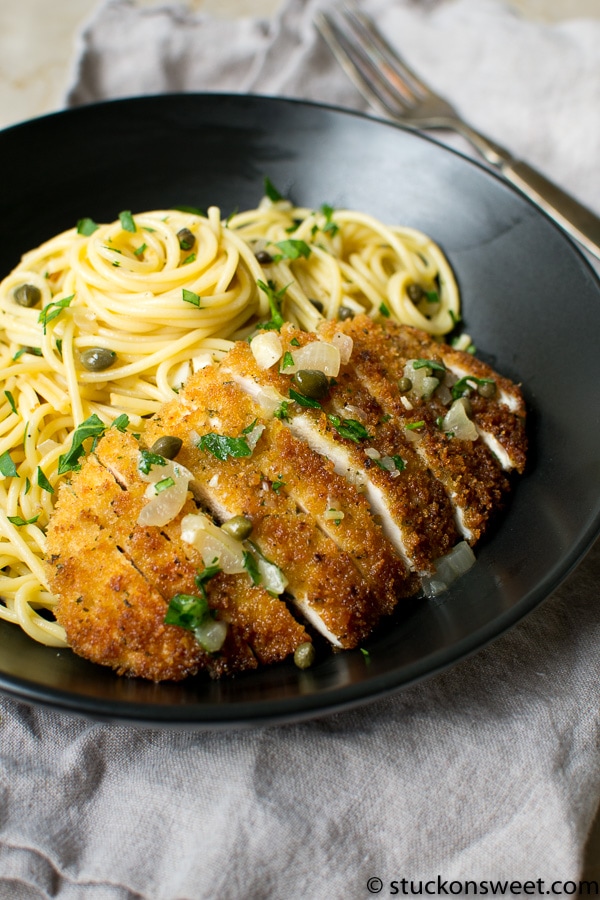 Crispy chicken piccata with lemon caper sauce served with spaghetti in a black bowl.
