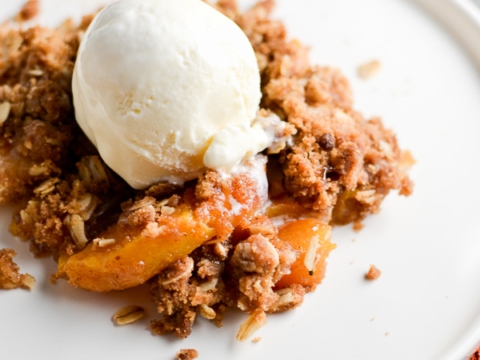 Sweet peach cobbler with vanilla ice cream served on a white plate, perfect for dessert or summer treat.