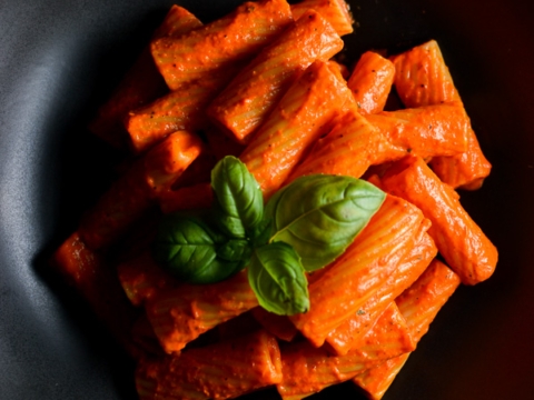 Sweet basil garnished pasta with tomato sauce in a black bowl, close-up shot.