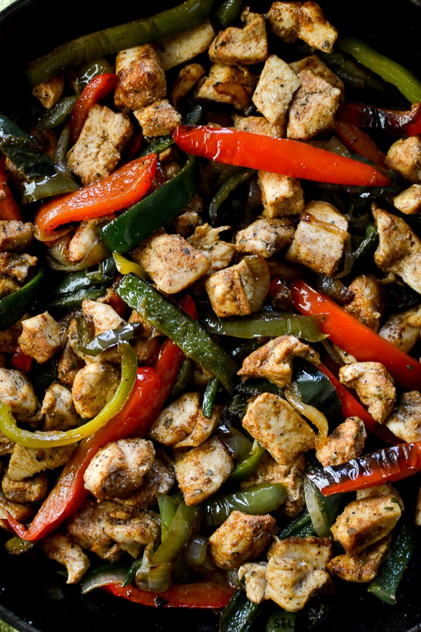 Sautéed chicken and colorful bell peppers stir-fry, perfectly seasoned with spices, on a black skillet. A healthy, delicious meal idea from Stuck On Sweet with fresh ingredients and vibrant flavors.