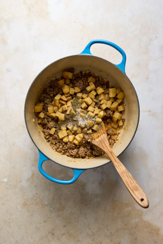 Image of Zuppa Toscana soup ingredients in a pot, including cooked sausage, diced potatoes, and seasonings, ready to be combined into a hearty, creamy soup.