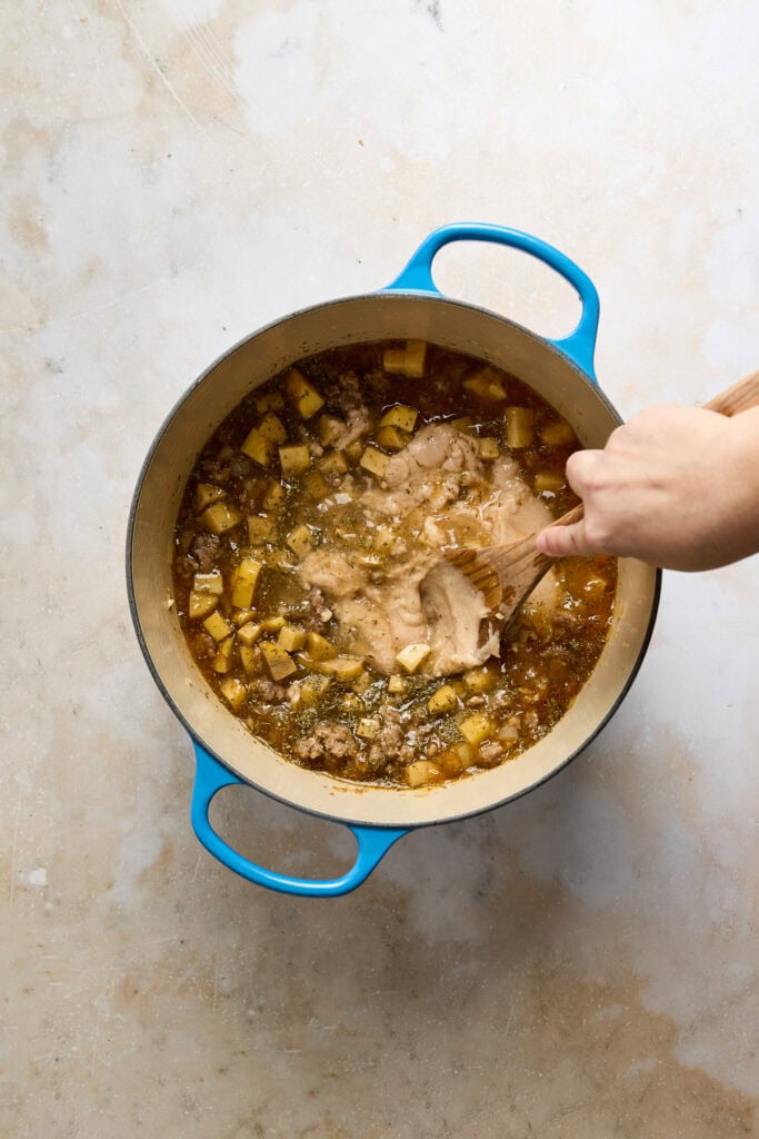Delicious Zuppa Toscana soup with potatoes, sausage, and kale simmering in a blue pot, perfect for a comforting meal. Ideal for fans of hearty, flavorful soups, this dish is a popular choice on Stuck.