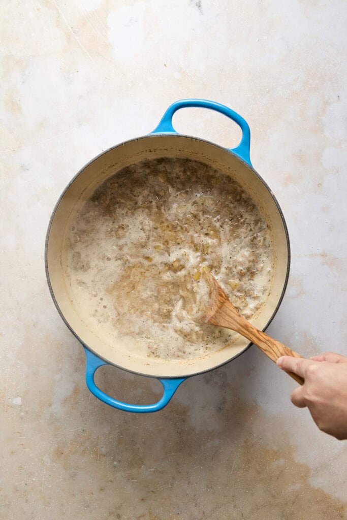 Creamy Zuppa Toscana soup in a blue cast iron skillet, featuring sausage, potatoes, kale, and cream, perfect for a comforting meal.