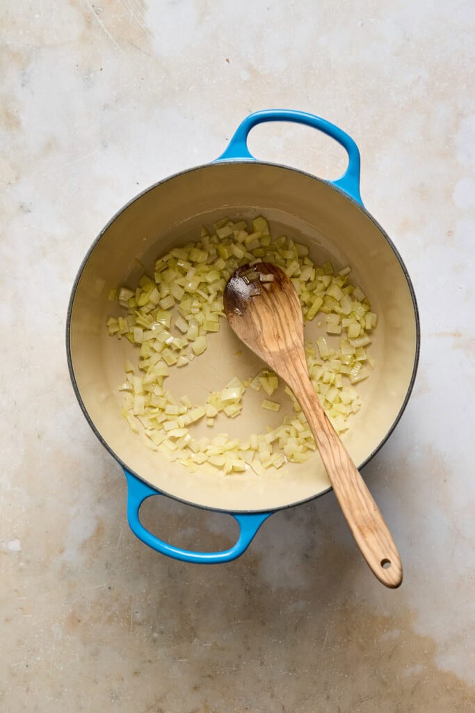 Image of chopped onions sautéing in a blue cast iron skillet, ready to be used in Zuppa Toscana soup recipe.