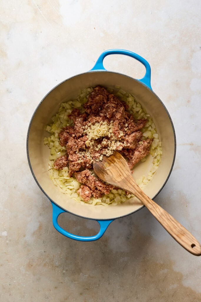 Cooking Zuppa Toscana soup with sausage, onions, garlic, and kale in a blue pot, ready to serve.