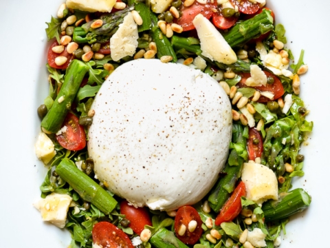 Creamy burrata cheese on a fresh vegetable salad with cherry tomatoes, green beans, pine nuts, and mozzarella on a white oval plate.