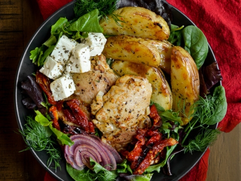 Crunchy grilled chicken with roasted potatoes, mixed greens, feta cheese, sun-dried tomatoes, and fresh herbs on a black plate for a healthy, flavorful meal.