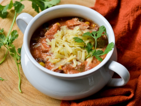Creamy tomato and cheese soup with fresh herbs in a white mug, served on a rustic wooden platter with garnishes; comforting homemade soup perfect for cold days.