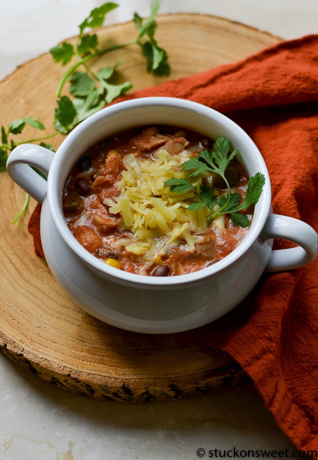 Creamy beef chili soup with shredded cheese and fresh cilantro in a white bowl on wooden serving board.