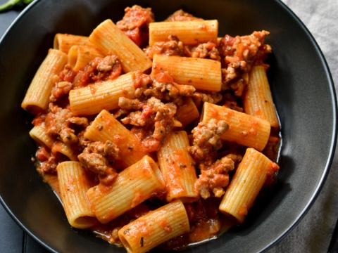 Rigatoni pasta with savory meat sauce on a black plate, close-up shot.