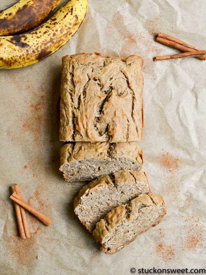 Banana bread sliced on parchment paper with cinnamon sticks and ripe bananas in the background, highlighting homemade baked goods and sweet breakfast ideas.