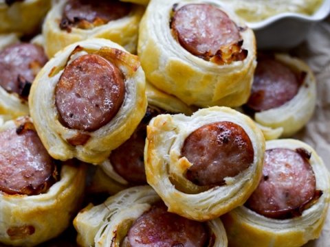 Savory ham and puff pastry wraps with cheese and mustard, served with creamy dipping sauce on a rustic wooden platter for appetizer or snack.