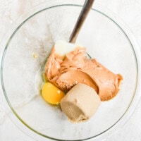 Cream cheese, peanut butter, egg yolk, and sugar in a glass mixing bowl for healthy no-bake dessert preparation.