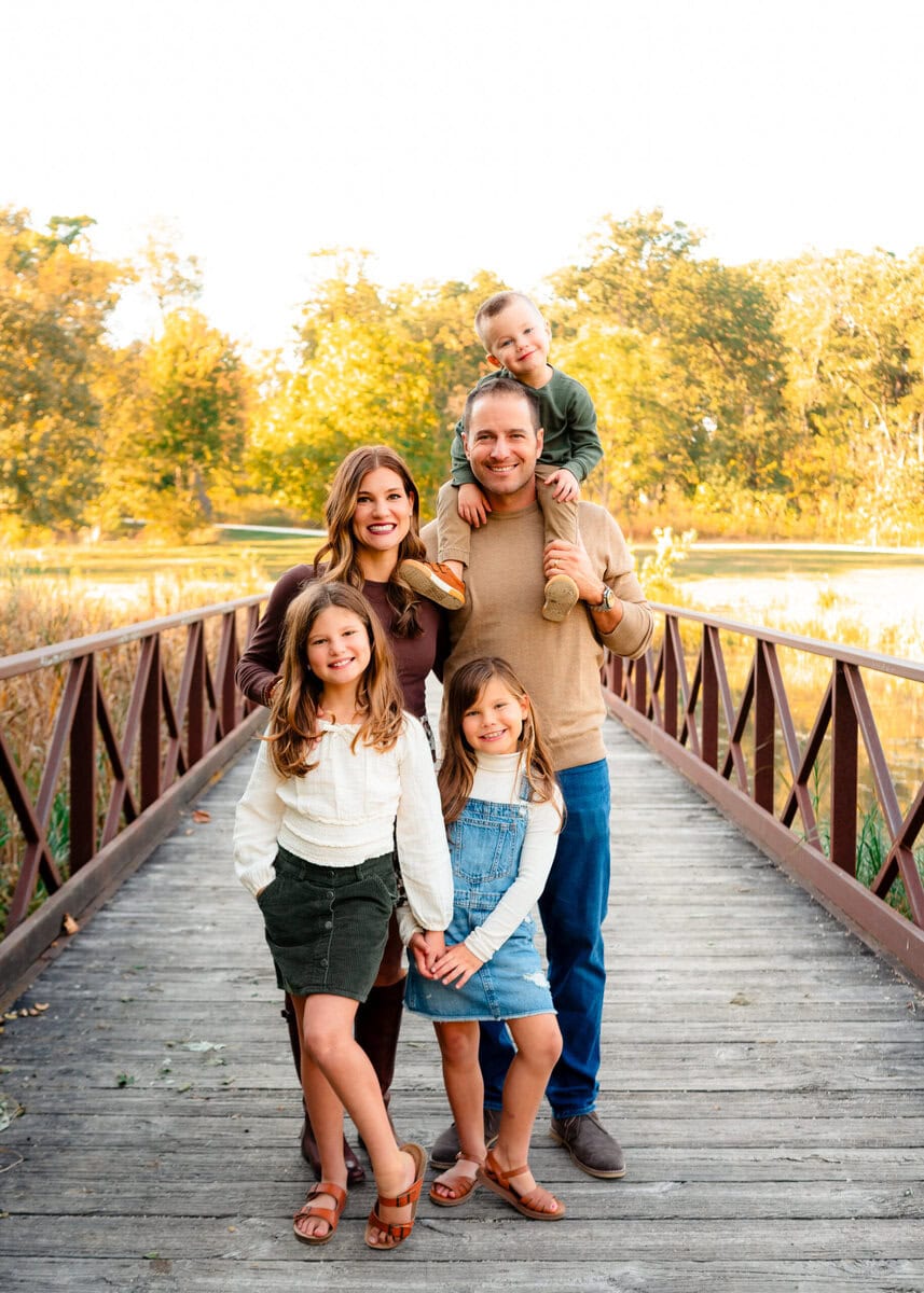 Family portrait on a bridge during fall, happy parents with children, autumn foliage, outdoor lifestyle photography.
