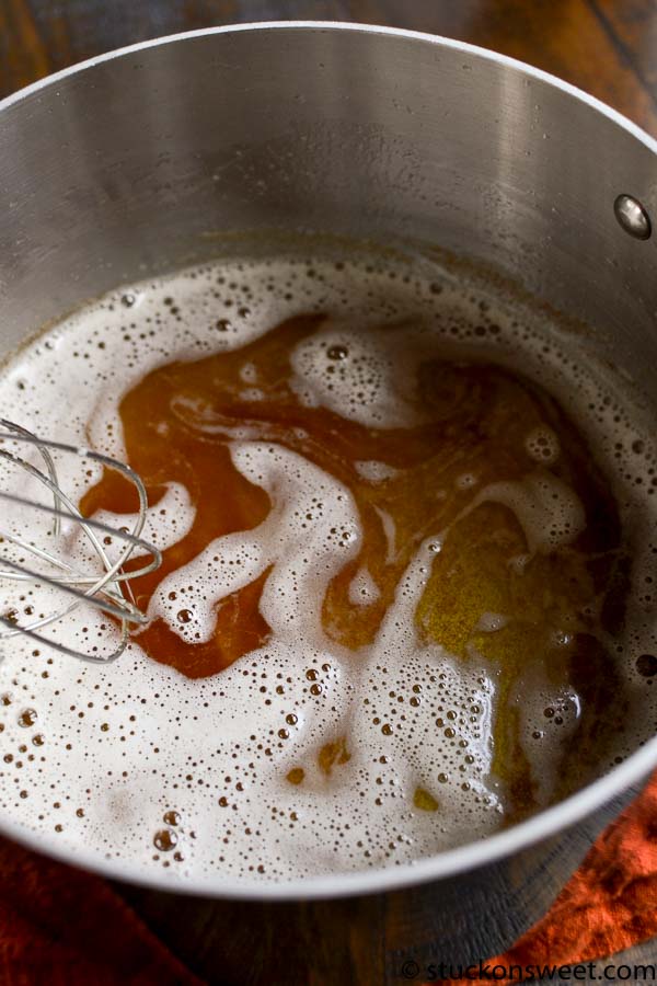 Golden caramel being heated and mixed in a stainless steel pot for candy making.