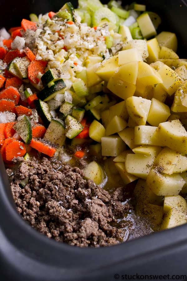 Diced potatoes, carrots, celery, and ground beef cooking in a slow cooker for a hearty meal. Fresh vegetables and seasoned meat ready for a comforting stew recipe.