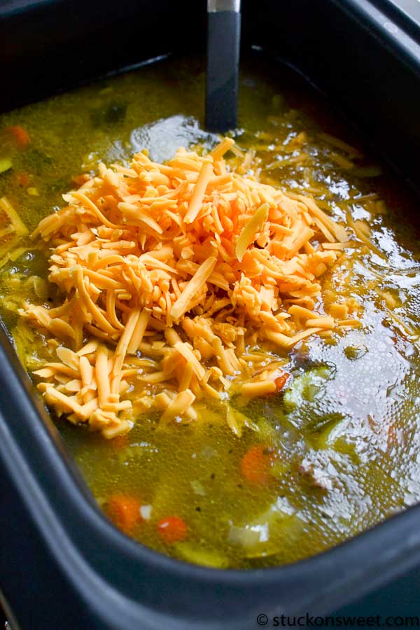 Shredded cheese melting in slow cooker with vegetable soup, easy cheesy soup recipe, comforting cheesy vegetable soup in crockpot, cheesy soup ingredients, slow cooker cheesy vegetable soup.