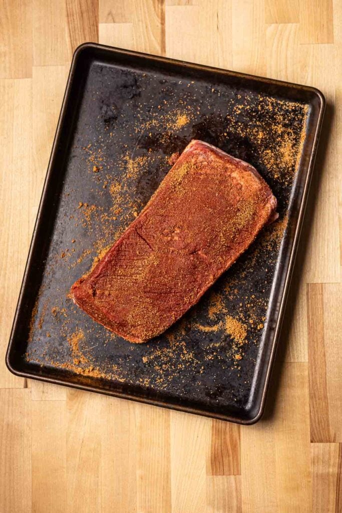 Juicy smoked brisket seasoned with spices on black baking sheet for BBQ or holiday meal at Stuck On Sweet.