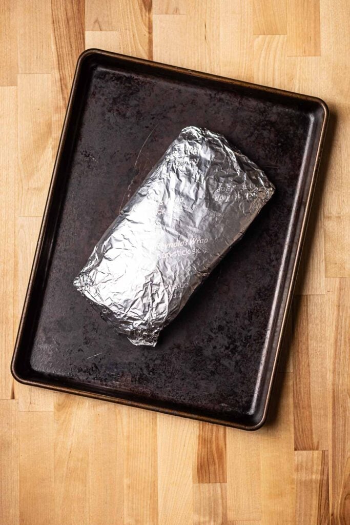 Foil-wrapped baked potato on a baking sheet with a wooden countertop.