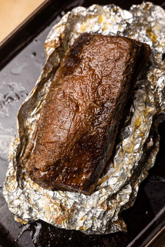 Delicious baked brisket wrapped in aluminum foil, topped with a savory, caramelized glaze, ready to serve. Perfect for slow-cooked barbecue and meat lovers.