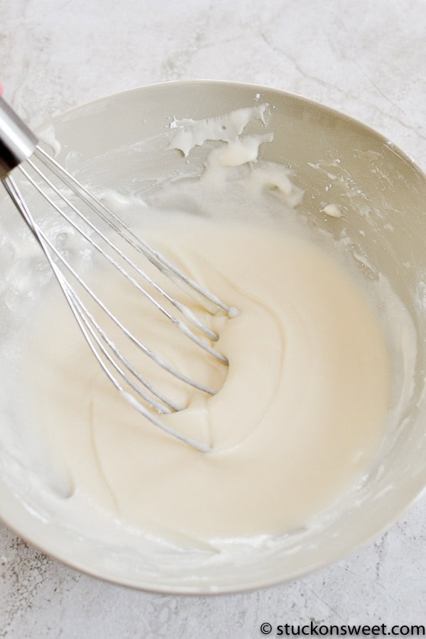 Creamy white cake batter mixed with a hand mixer in a white bowl.
