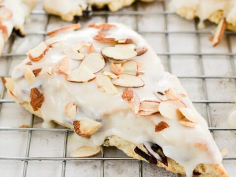 Almond Croissant Danish pastry with white icing and sliced almonds on wire rack.