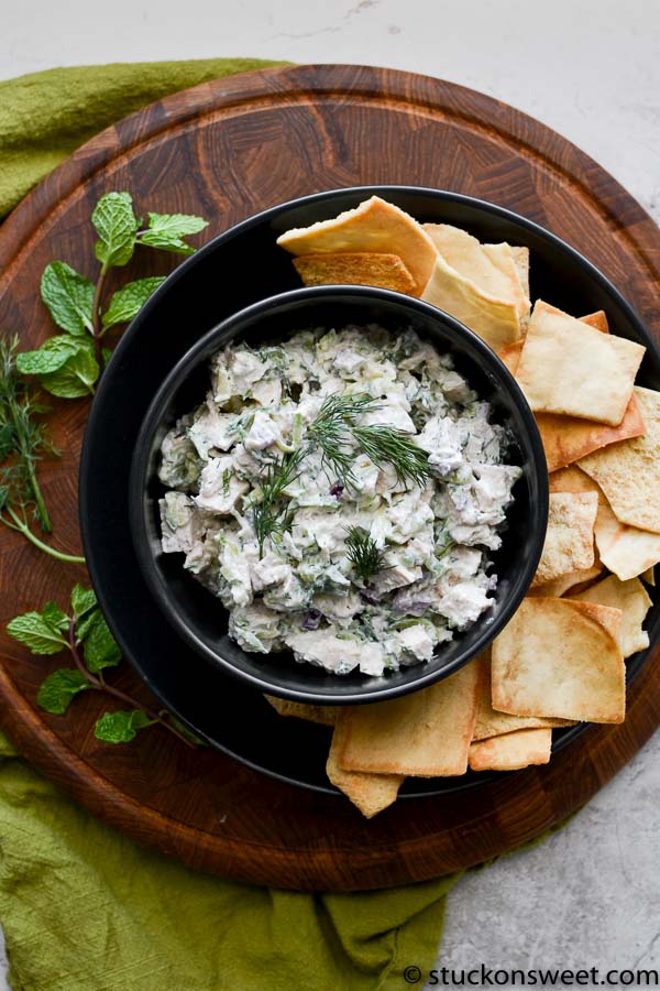 Creamy chicken salad dip garnished with fresh herbs served with crispy pita chips and flatbread on a wooden platter, perfect for parties and snack platters.