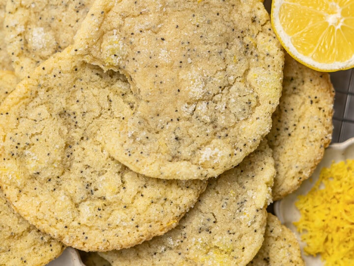 Freshly baked lemon poppy seed cookies garnished with fresh lemon slices and served with vanilla and lemon zest on a cooling rack. Perfect for sweet lemon lovers and lemon-themed desserts.
