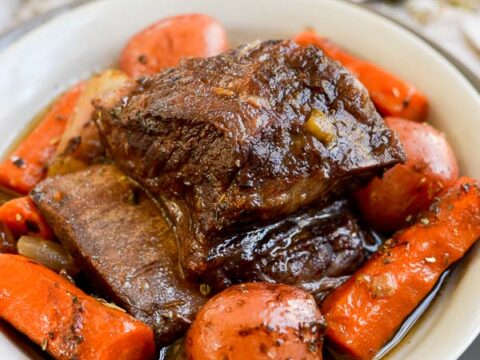 Braised beef short ribs with carrots and potatoes in a rich, savory sauce served in a white bowl. Perfect comfort food for dinner or special occasions.