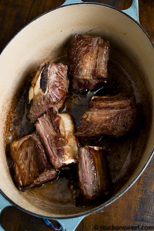 Braised beef short ribs in a Dutch oven, slow cooked beef ribs, savory beef pot roast, hearty comfort food, tender meat recipe.