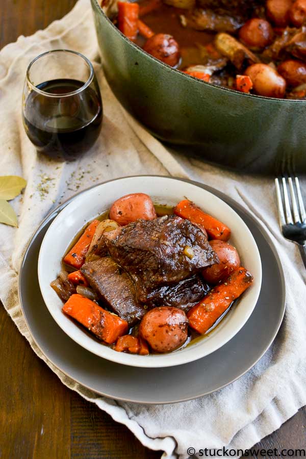 Juicy pot roast with carrots and potatoes served with a glass of red wine on a rustic table.