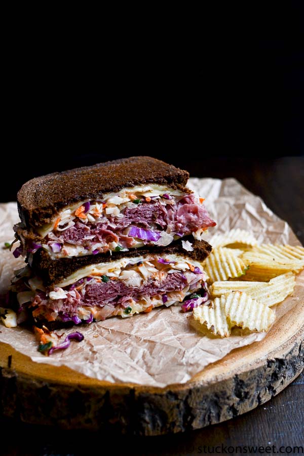 Crispy breaded sandwich with corned beef, coleslaw, and potato chips on a wooden serving board.