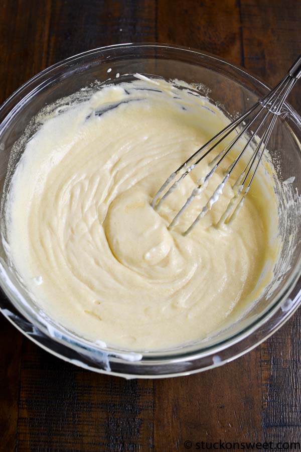 Creamy cake batter in a glass mixing bowl with a whisk attachment, ready for baking.