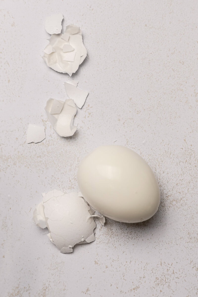 White chicken egg with cracked shells on a light textured background, emphasizing fresh eggs for baking and cooking, ideal for culinary and kitchen related content.