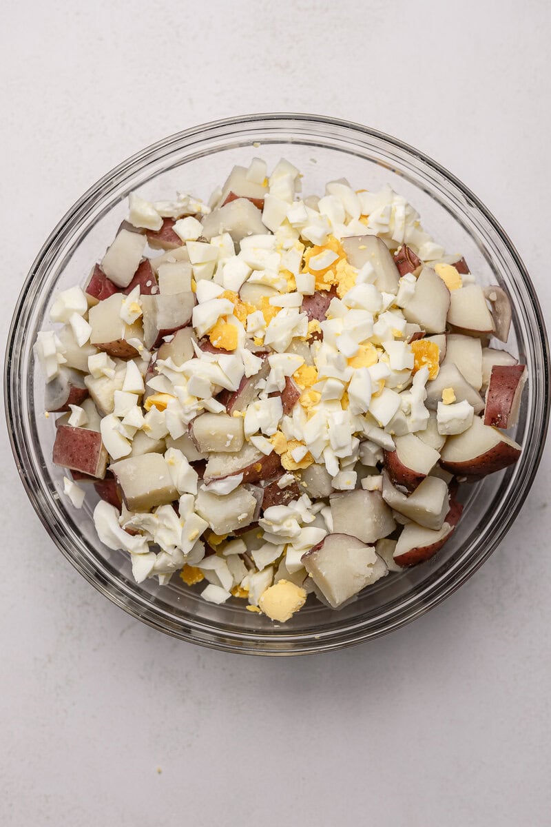 Diced potatoes and hard-boiled eggs in a glass bowl, prepared for potato salad or casserole. Fresh ingredients ideal for savory potato-based dishes, showcasing a close-up view for recipe inspiration.