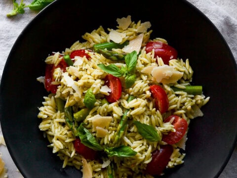 Creamy pesto pasta with cherry tomatoes, fresh basil, and shaved Parmesan cheese on a black plate. Perfect for a quick, delicious vegetarian meal. garnished with lemon slices and basil leaves.