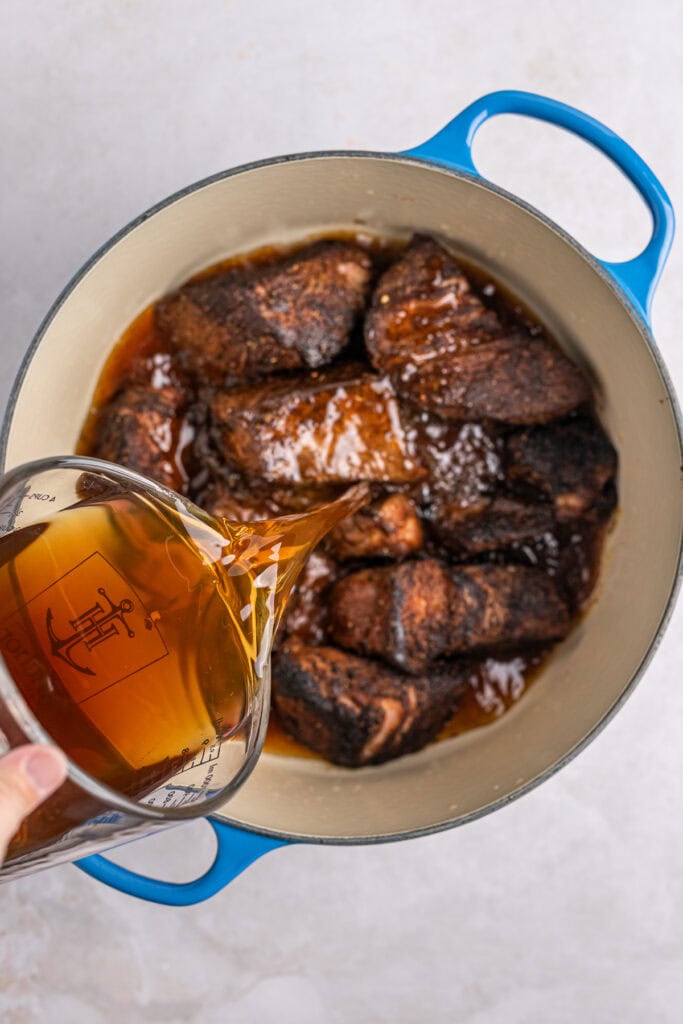 Rich caramelized beef stew in a blue Dutch oven with dark gravy and tender meat pieces.