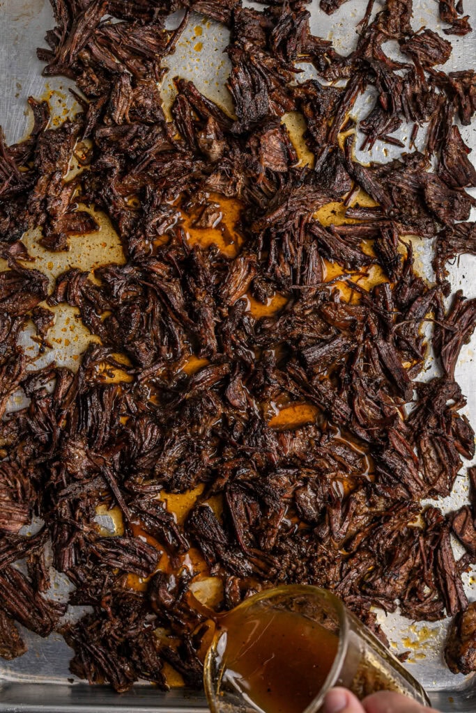 Shredded beef brisket cooked with barbecue sauce on a baking sheet, with juice and seasoning visible. Perfect for making sandwiches, tacos, or dinner recipes.