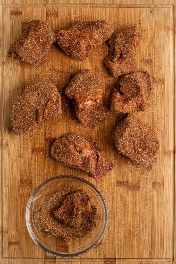 Crispy seasoned fried chicken pieces on a wooden cutting board with a small bowl of seasoned coating. Perfect for comfort food, fried chicken recipes, and spicy chicken dishes.
