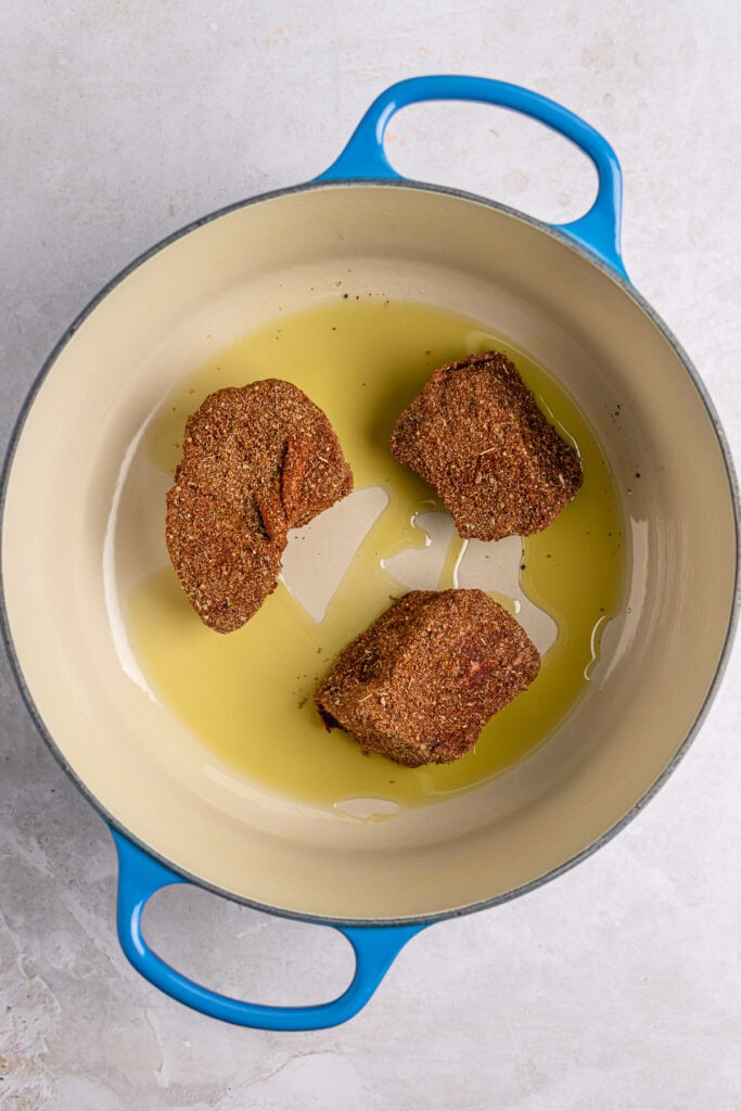 Crispy breaded meatloaf in olive oil inside a white ceramic skillet with a blue handle.
