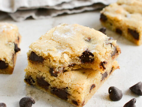 Buttery chocolate chip cookie bars with melted chocolate chunks and a golden crisp, served on a white surface for delicious homemade baking desserts.