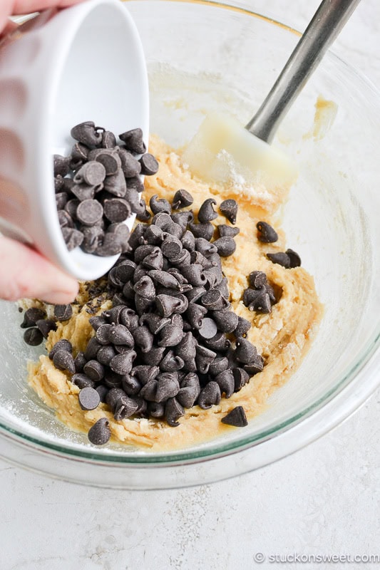 Chocolate chips being added to cookie dough in a mixing bowl for baking.