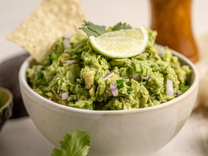 Creamy avocado salad garnished with lime wedge and cilantro in a white bowl. Topped with red onion and served with crispy tortilla chips, perfect for healthy snacking and guacamole recipes.