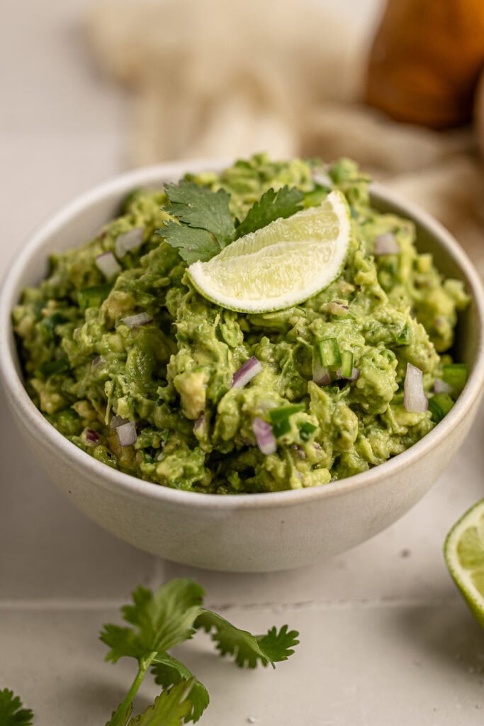 Creamy avocado guacamole with lime wedge and cilantro in a white bowl, fresh and delicious Mexican-inspired dip, perfect for snacks and parties.