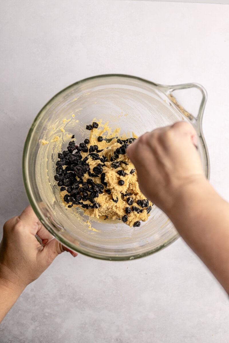 Creamy cookie dough with chocolate chips in a glass mixing bowl, being stirred by hand, perfect for homemade cookie recipes and sweet treats.
