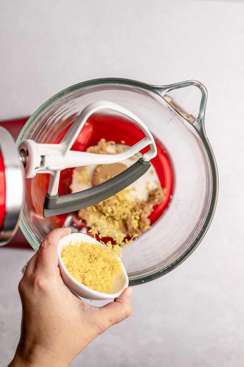 Cream cheese being mixed with lemon zest in a glass bowl with an electric mixer, preparing sweet frosting or filling.