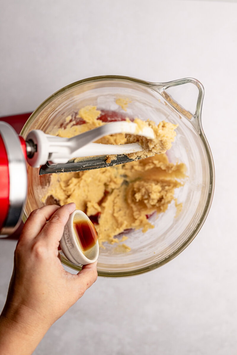 Cream cookie dough with vanilla and brown sugar in a glass mixing bowl, using a hand mixer, with vanilla extract added, for homemade cookie recipes.