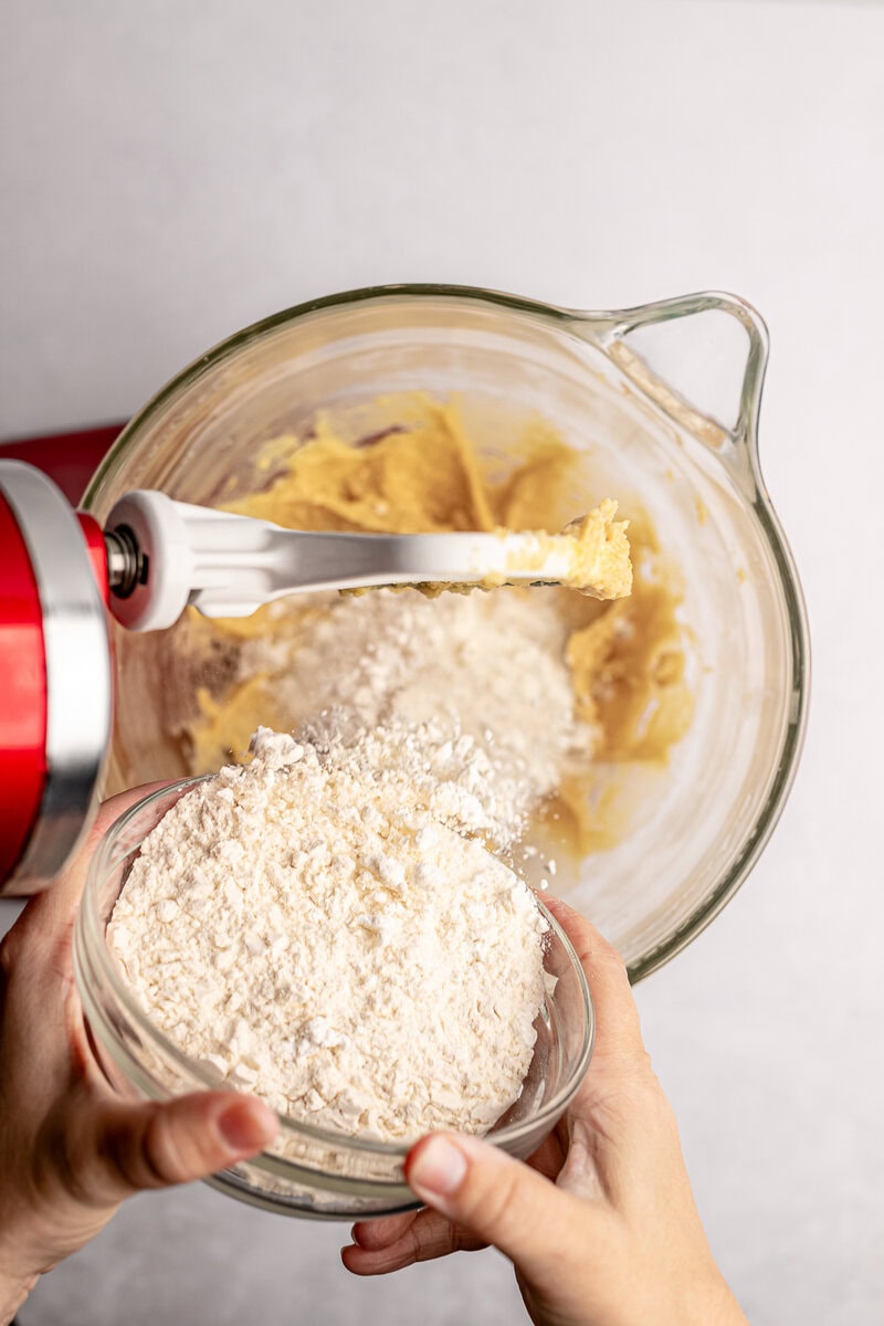 Creamy yellow cake batter with flour being added from a bowl for baking.